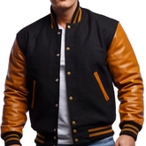 A man wearing a black and brown varsity jacket with leather sleeves and wool body, featuring a V-neck collar and metal buttons.